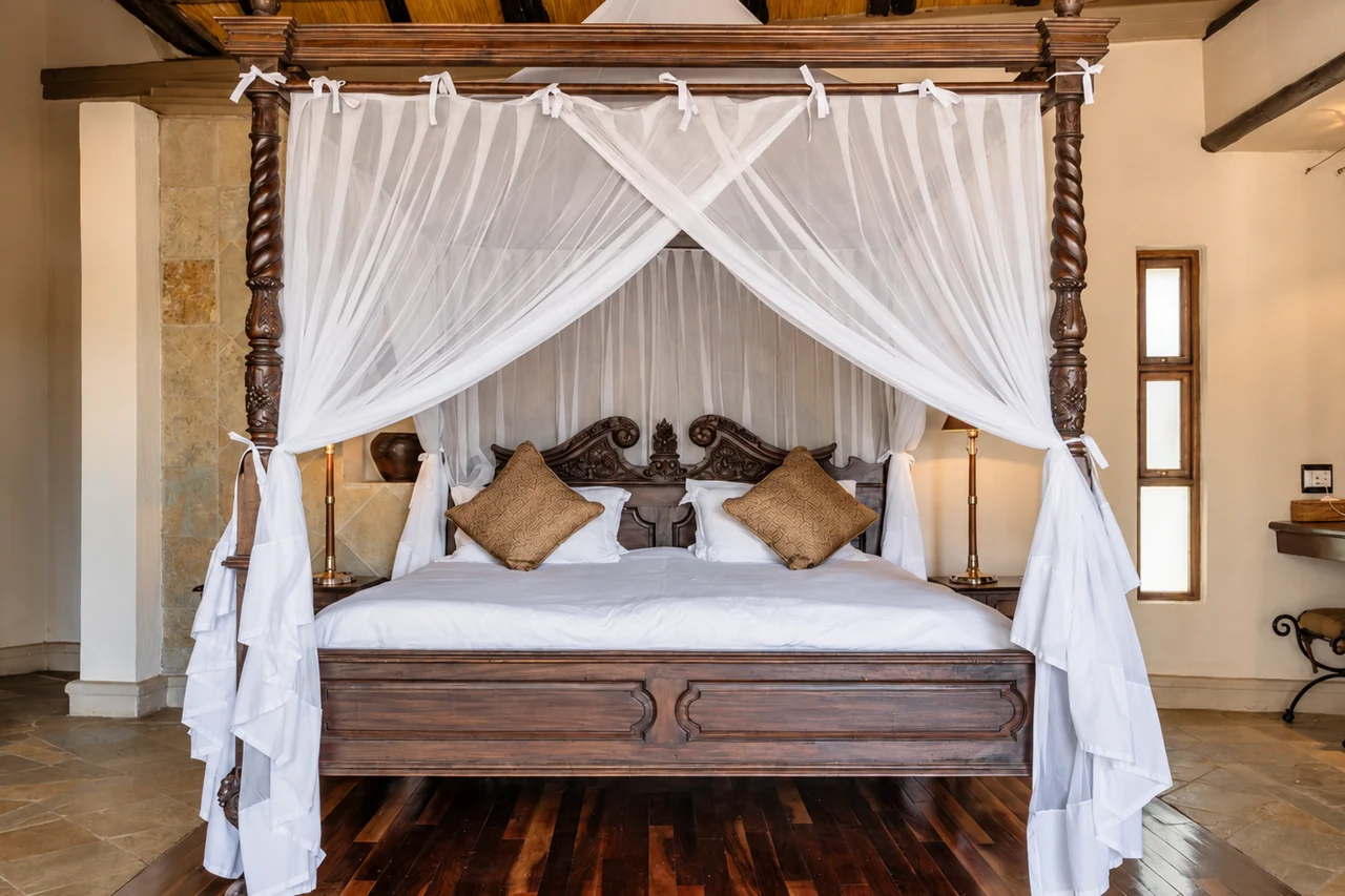 White mosquito netting tied around a carved wooden four-poster bed.