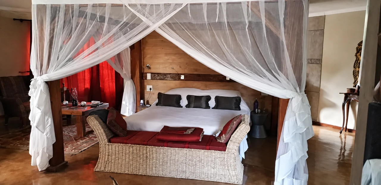 A wide canopy of white netting draped around a bed with red cushions.