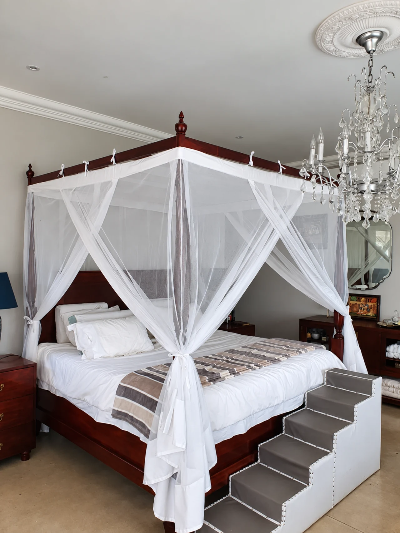 A white mosquito net tied to the corners of a dark four-poster bed.